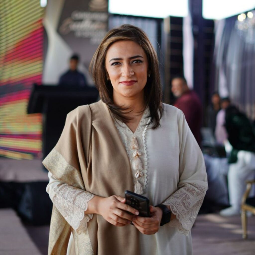 Elegant businesswoman holding smartphone, smiling at an event in Dubai. Professional attire and warm ambiance.